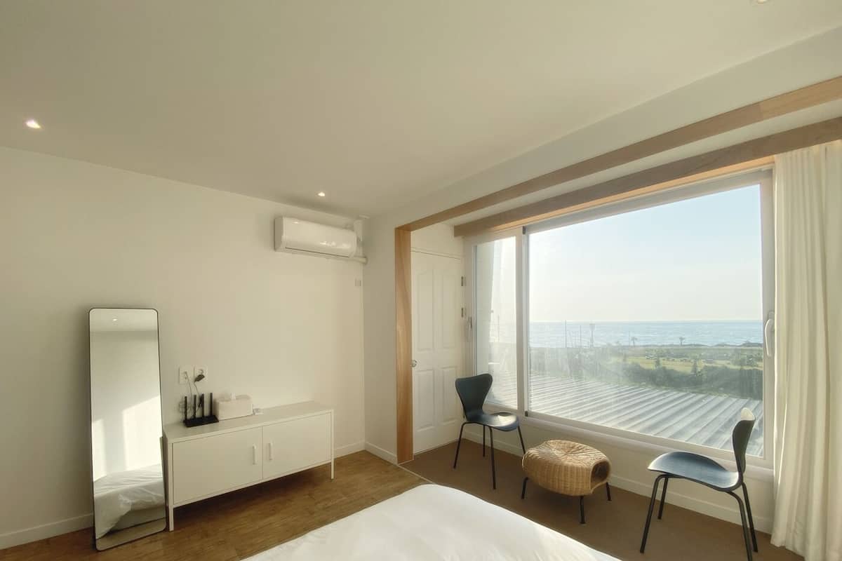 Een moderne hotelkamer met een groot bed, nachtkastje, spiegel, stoel en uitzicht op zee.