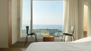 A bedroom with a large sliding glass door leading to a balcony overlooking the sea. There are two chairs and a small woven stool on the balcony. - Gongzonestay (Jeju City)