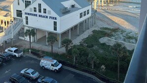 Un edificio blanco llamado 'Surfside Beach Pier' con un estacionamiento y un muelle que se adentra en el agua.