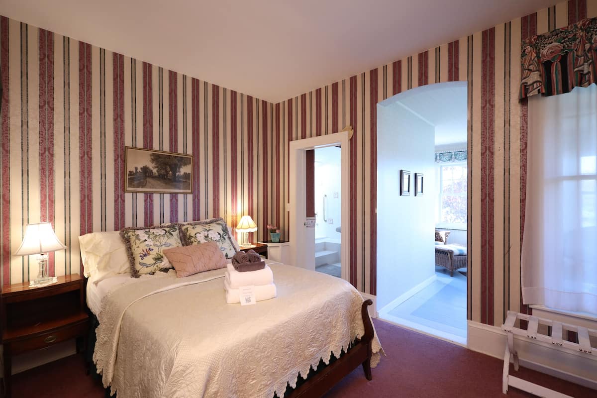 Ein Hotelzimmer mit einem großen Bett, Streifen-Tapete, einem Bild an der Wand und Blick nach draußen.