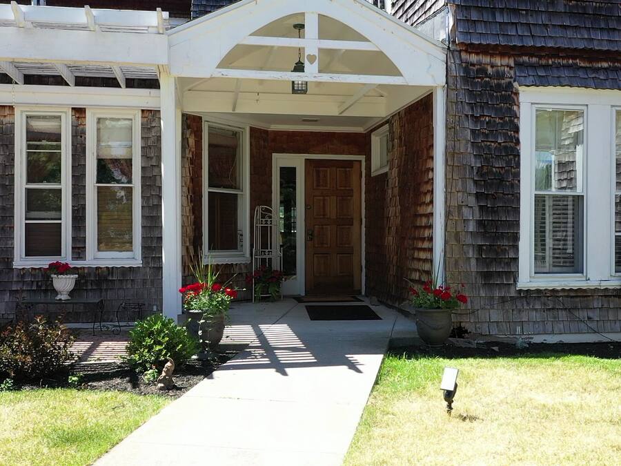 A two-story house with a covered front porch, a wooden door, and a small garden with red flowers.