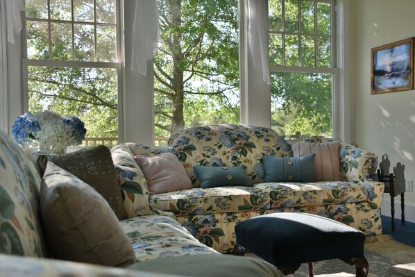 A cozy living room with a floral sofa, a matching ottoman, and a vase of flowers. - Thousand Island Hart House (Wellesley Island)