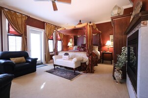 Quarto com cama de dossel, área de estar com sofá e poltrona, e lareira.