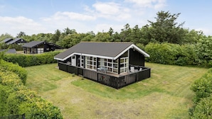 Een modern huis met een groot terras, omgeven door verzorgde gazons en weelderige begroeiing.