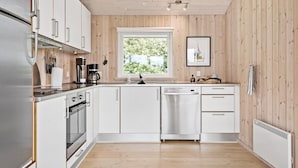 Een moderne keuken met witte kastjes, roestvrijstalen apparatuur en een raam met uitzicht op groen.