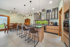 A modern kitchen with a central island, bar stools, pendant lighting, and built-in cabinetry. - Stanley Stay | 3BR · Sauna & Playset, Pet-Friendly (Woodville Park)