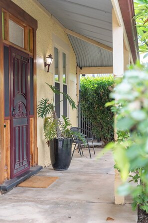 A covered porch with a potted plant, a chair, and a door with a decorative design. - Stanley Stay | 3BR · Sauna & Playset, Pet-Friendly (Woodville Park)