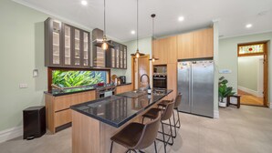 A modern kitchen with a central island, bar stools, stainless steel appliances, and a large fish tank.