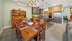 A modern kitchen with wooden cabinets, a stainless steel refrigerator, and a dining area with a wooden table and chairs.