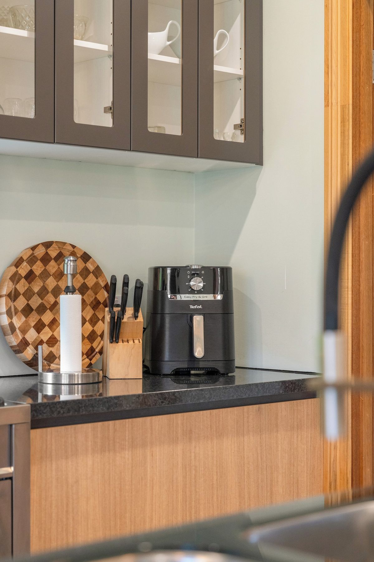 A kitchen with a coffee maker, a knife block, and a checkered cutting board.