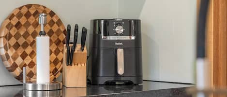 Una cocina con cafetera, bloque de cuchillos y tabla de cortar a cuadros.