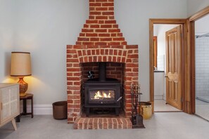 A brick fireplace with a modern wood-burning stove, a lamp on a side table, and a wooden door in the background. - Stanley Stay | 3BR · Sauna & Playset, Pet-Friendly (Woodville Park)
