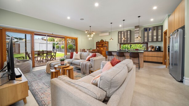 A spacious living room with a sofa, coffee table, and TV, connected to a kitchen with a refrigerator and cabinets.