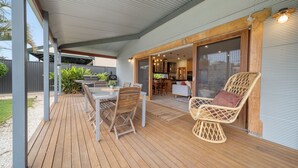 A covered outdoor patio with a wooden deck, a dining table with chairs, and a wicker chair.