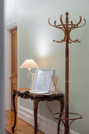 Et træstående klædestativ med et velkomstskilt, en lampe og et bord med en bærbar computer og papirer.