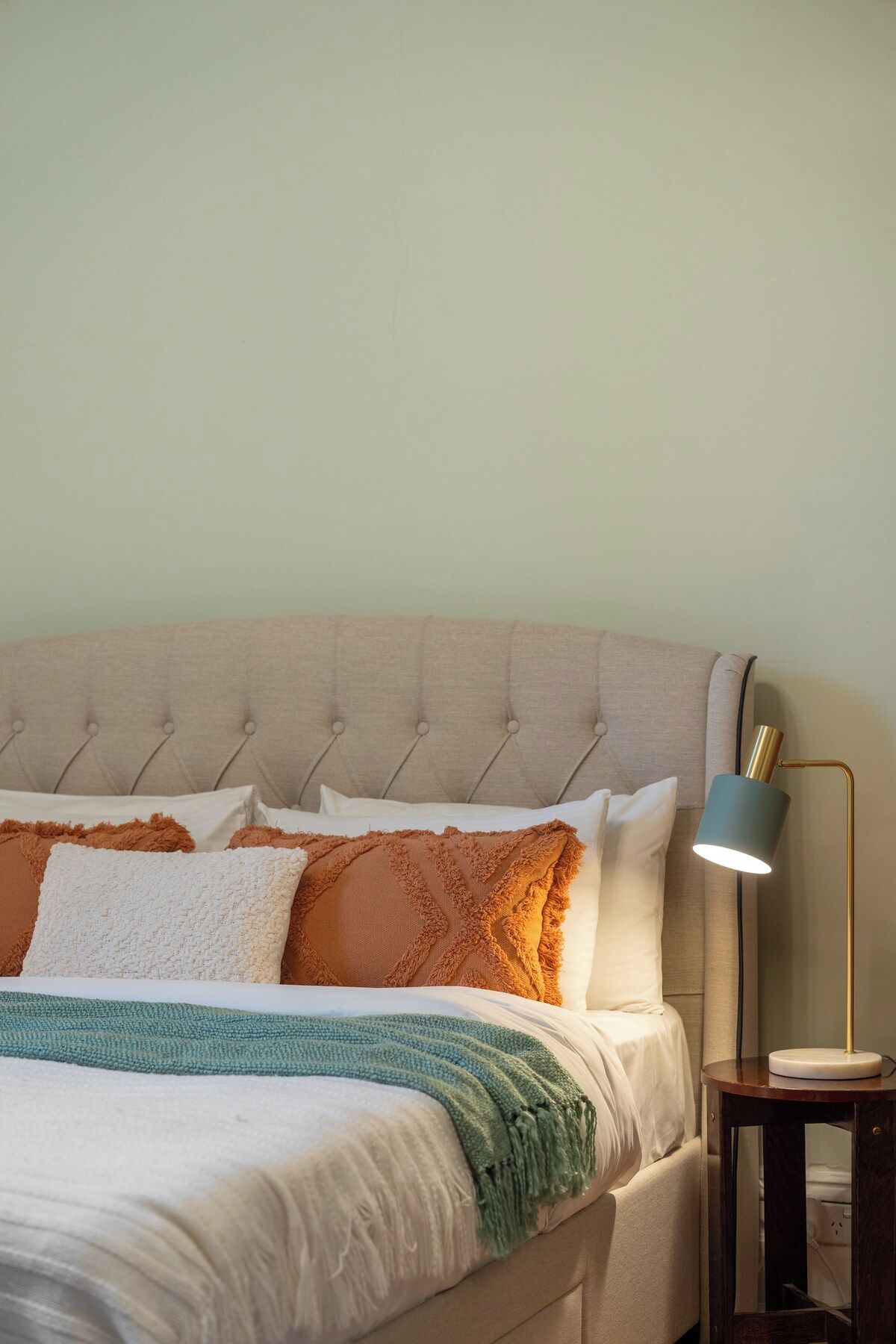 A bed with a tufted headboard, multiple pillows, and a bedside lamp.