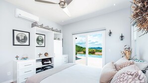 Une chambre dotée d’un grand lit, d’une armoire, d’un ventilateur de plafond et offrant une vue sur un paysage verdoyant grâce à une porte coulissante.