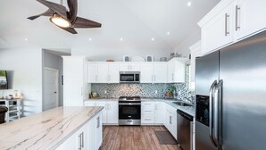 Une cuisine moderne avec des meubles blancs, un réfrigérateur en acier inoxydable, un four à micro-ondes et un plancher en bois.