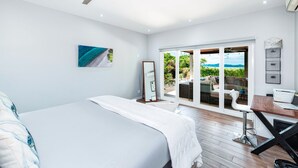Une chambre à coucher avec un lit, un ventilateur de plafond, une grande fenêtre et une vue sur l’extérieur.