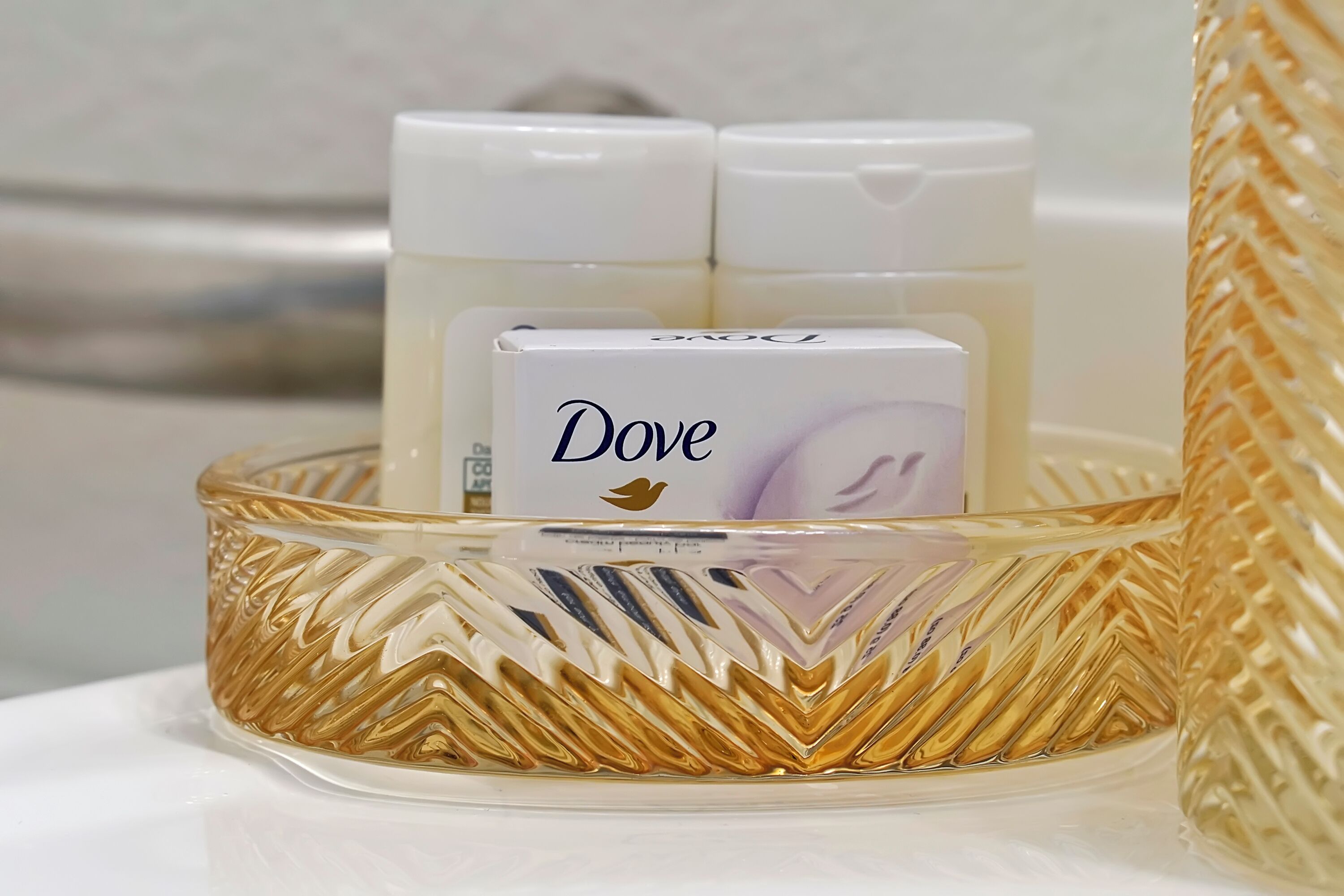 Uma bandeja de vidro com um produto Dove, um recipiente branco e uma garrafa branca.