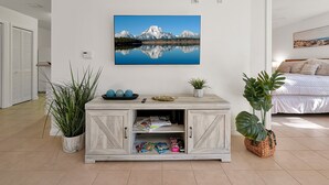 Un salon moderne avec un grand tableau représentant un lac de montagne, un meuble en bois contenant des magazines et deux plantes en pot.