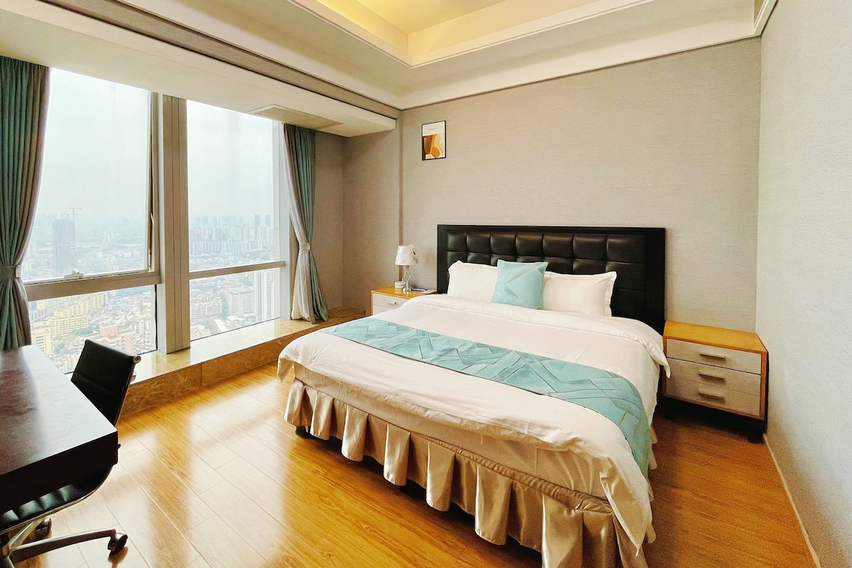 A hotel room with a large bed, a wooden desk, and a view of the city through the window.
