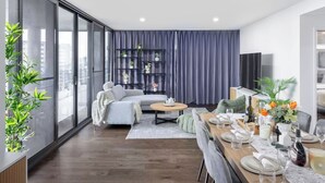 A modern living room with a sofa, dining table, and a large window. - Cityview 4 Beds/FR Carpark/pool at South Bank (South Brisbane)