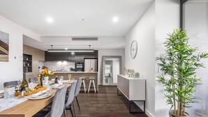 A modern dining area with a long wooden table, grey chairs, and a potted plant. - Cityview 4 Beds/FR Carpark/pool at South Bank (South Brisbane)