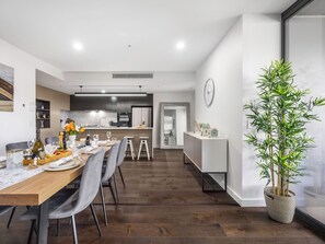 A modern dining area with a long wooden table, grey chairs, and a potted plant.