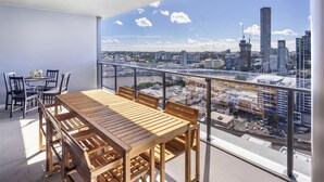 A balcony with a wooden table and chairs, overlooking a cityscape with buildings and a bridge. - Cityview 4 Beds/FR Carpark/pool at South Bank (South Brisbane)