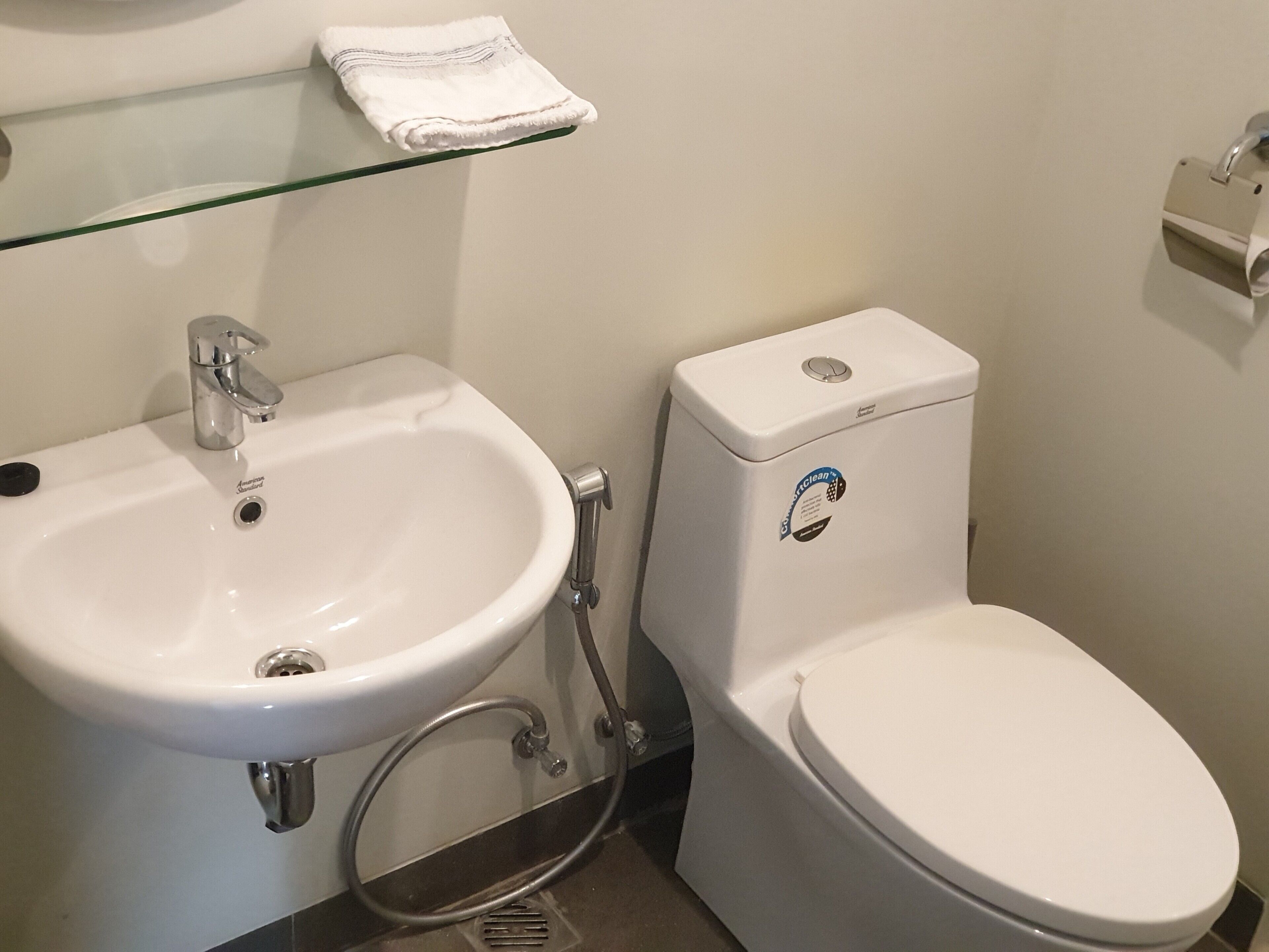 Un baño con lavamanos blanco, un inodoro y una repisa de vidrio sobre el lavamanos.
