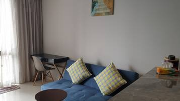 Una sala moderna con un sofá azul, dos cojines cuadriculados, una pequeña mesa redonda, una mesa de comedor con sillas y un cuadro en la pared.