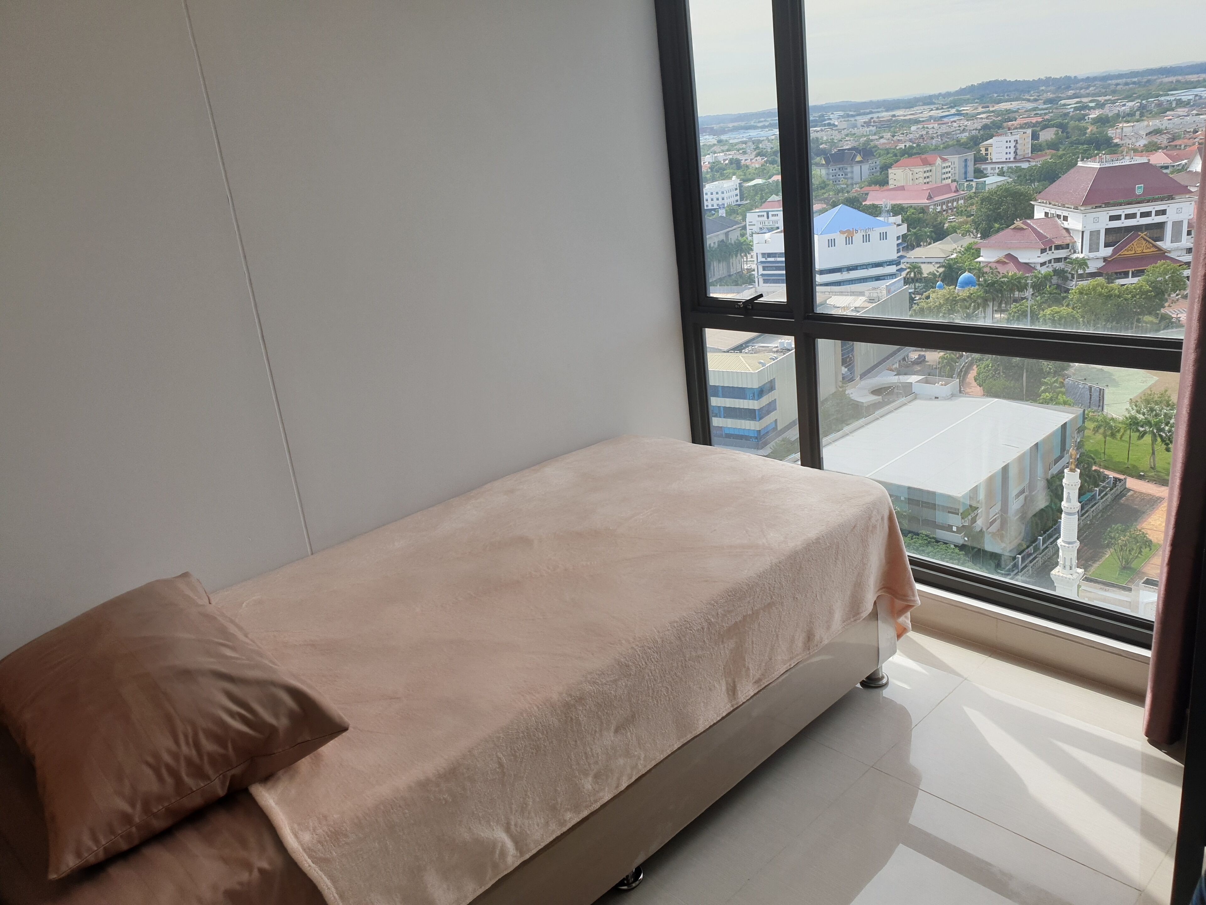 A room with a bed, a window, and a view of buildings.