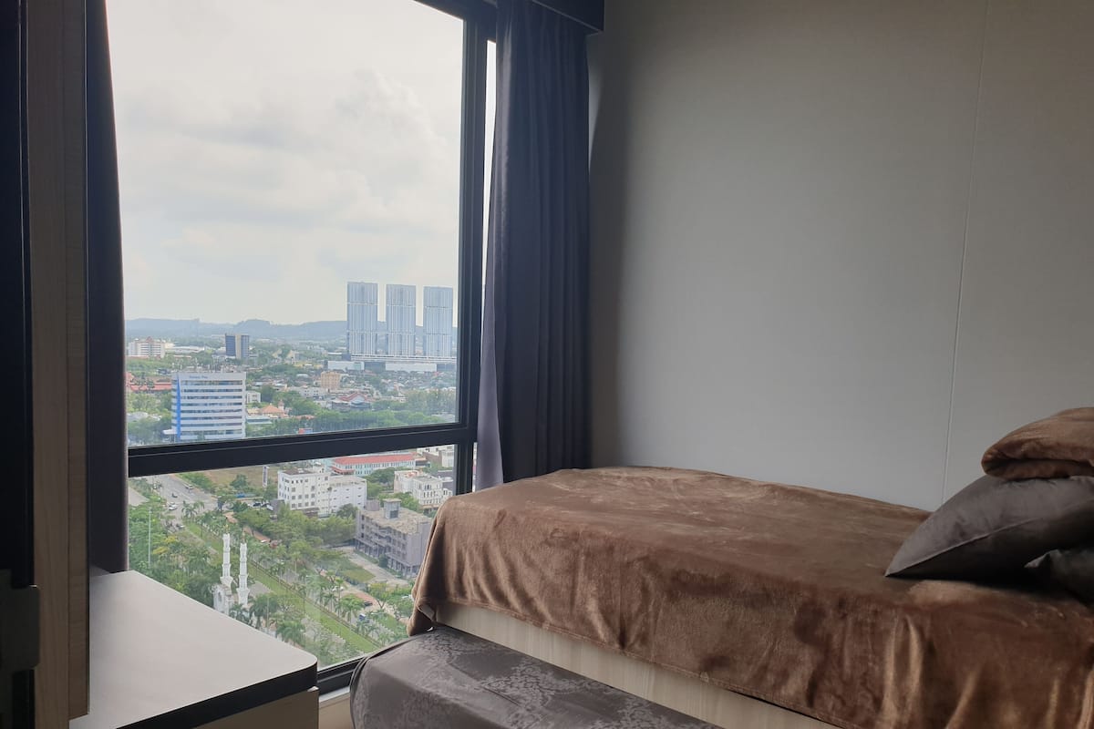 Ein Schlafzimmer mit einem Bett, einem Nachttisch und einem Fenster mit Blick auf die Stadt.