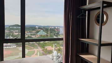 A hotel room with a large window offering a view of a cityscape, including a mosque and a building with a sign that reads "WELCOME TO BAT".