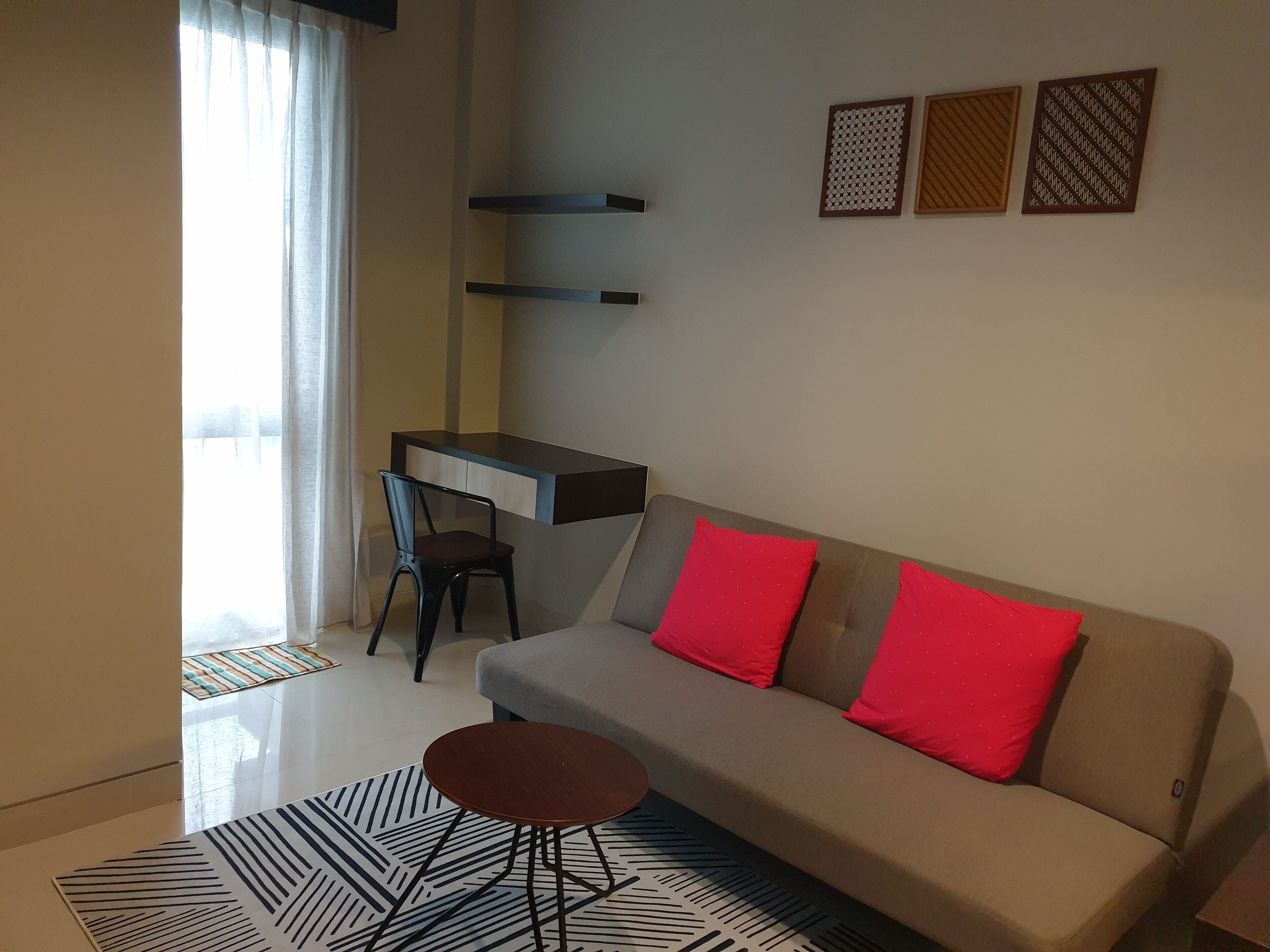 A modern living room with a sofa, a small round table, a desk, and a chair. There are three decorative panels on the wall.