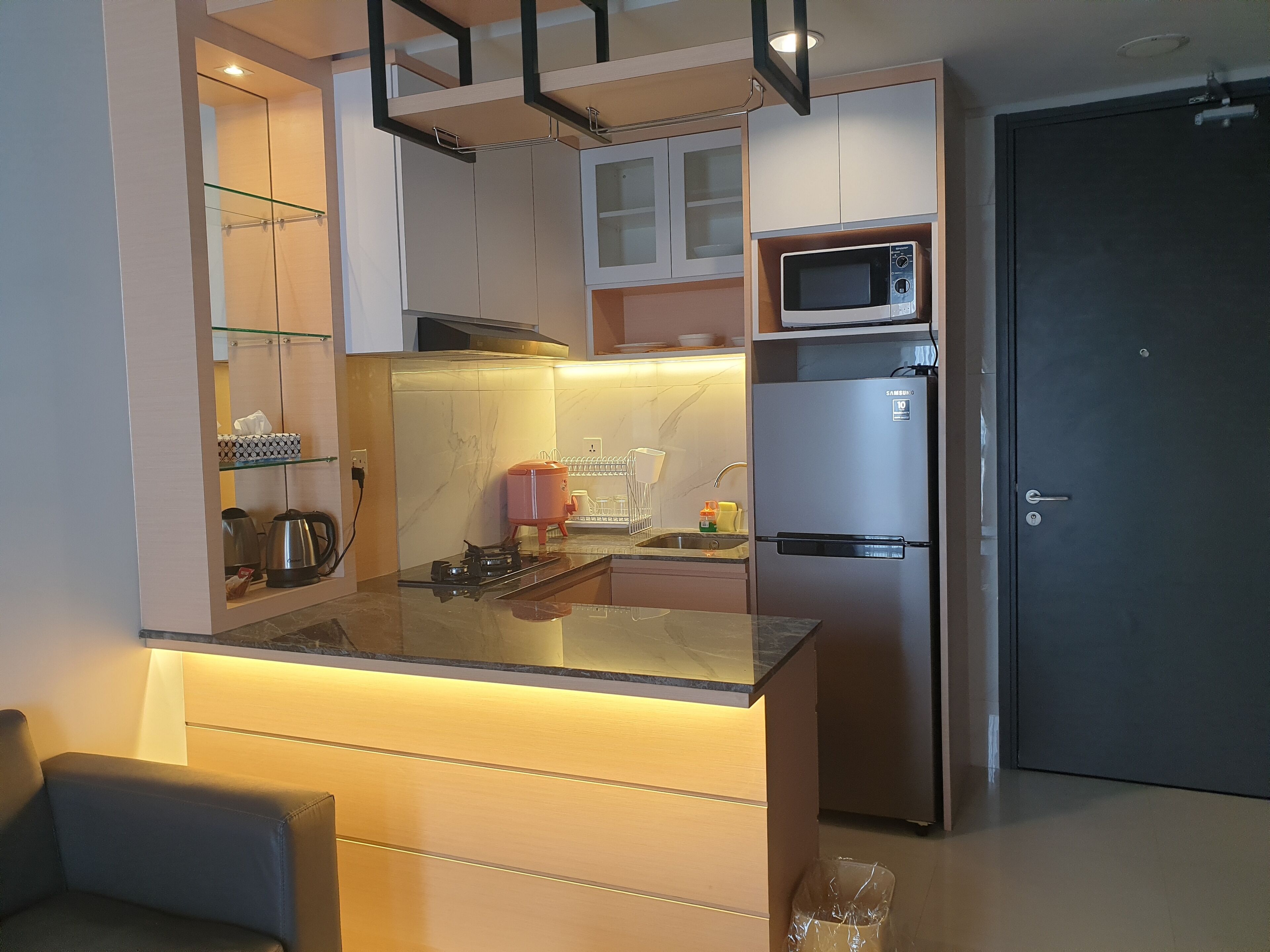 A modern kitchen with a built-in microwave, stainless steel refrigerator, and a glass island counter.