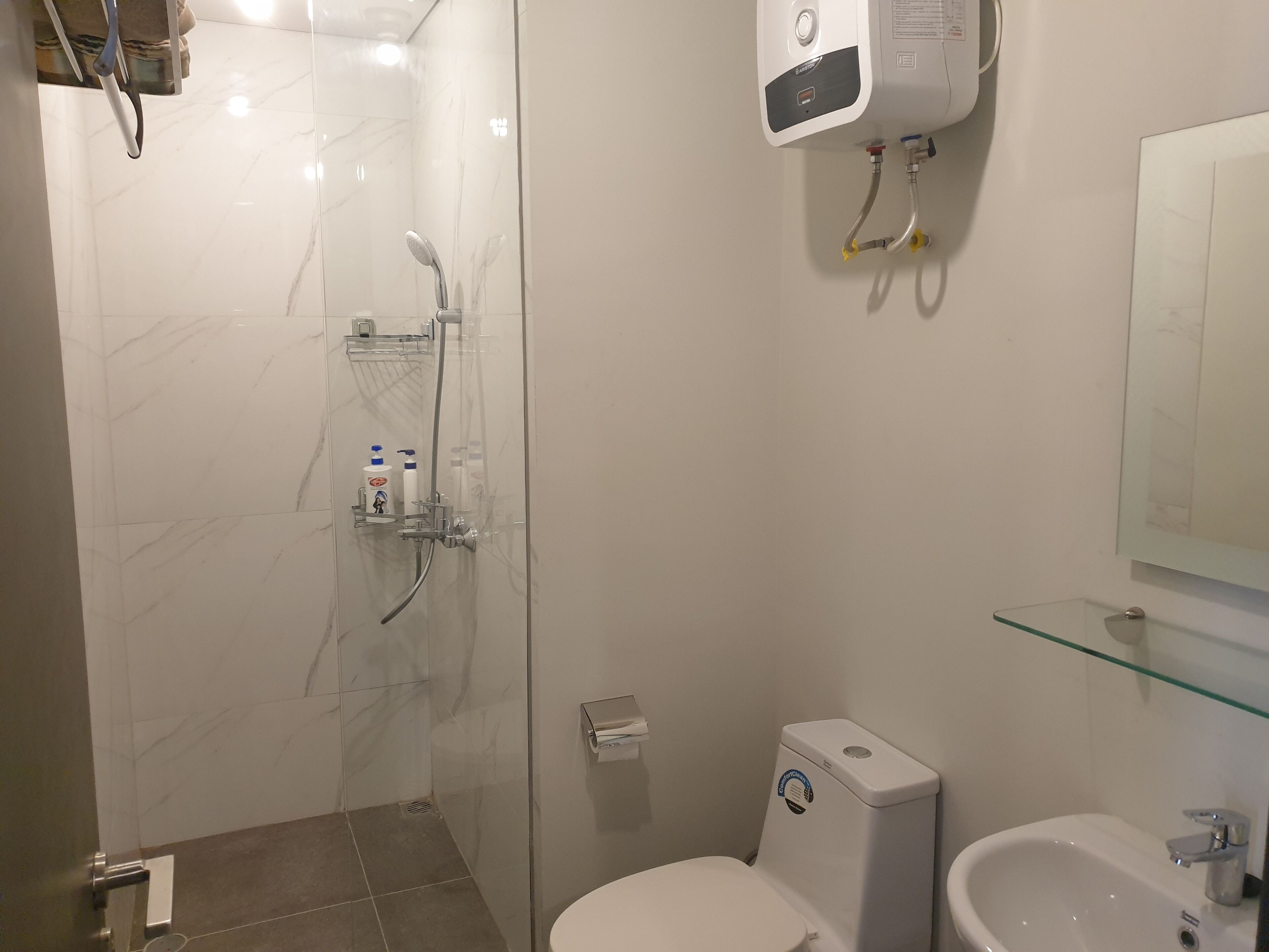 A bathroom with a shower, toilet, bidet, and a glass shelf.