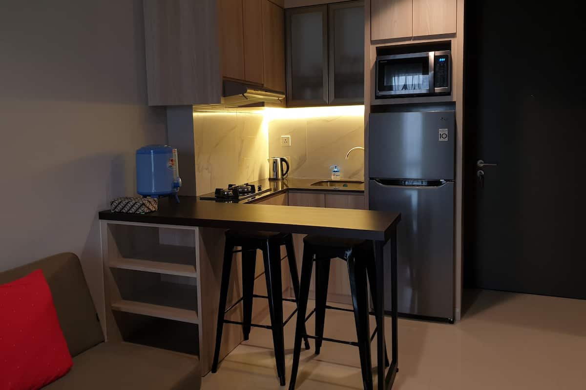 Eine kompakte Küche mit integriertem Mikrowellenherd, einem Edelstahl-Kühlschrank und einer kleinen Essecke mit Hocker.
