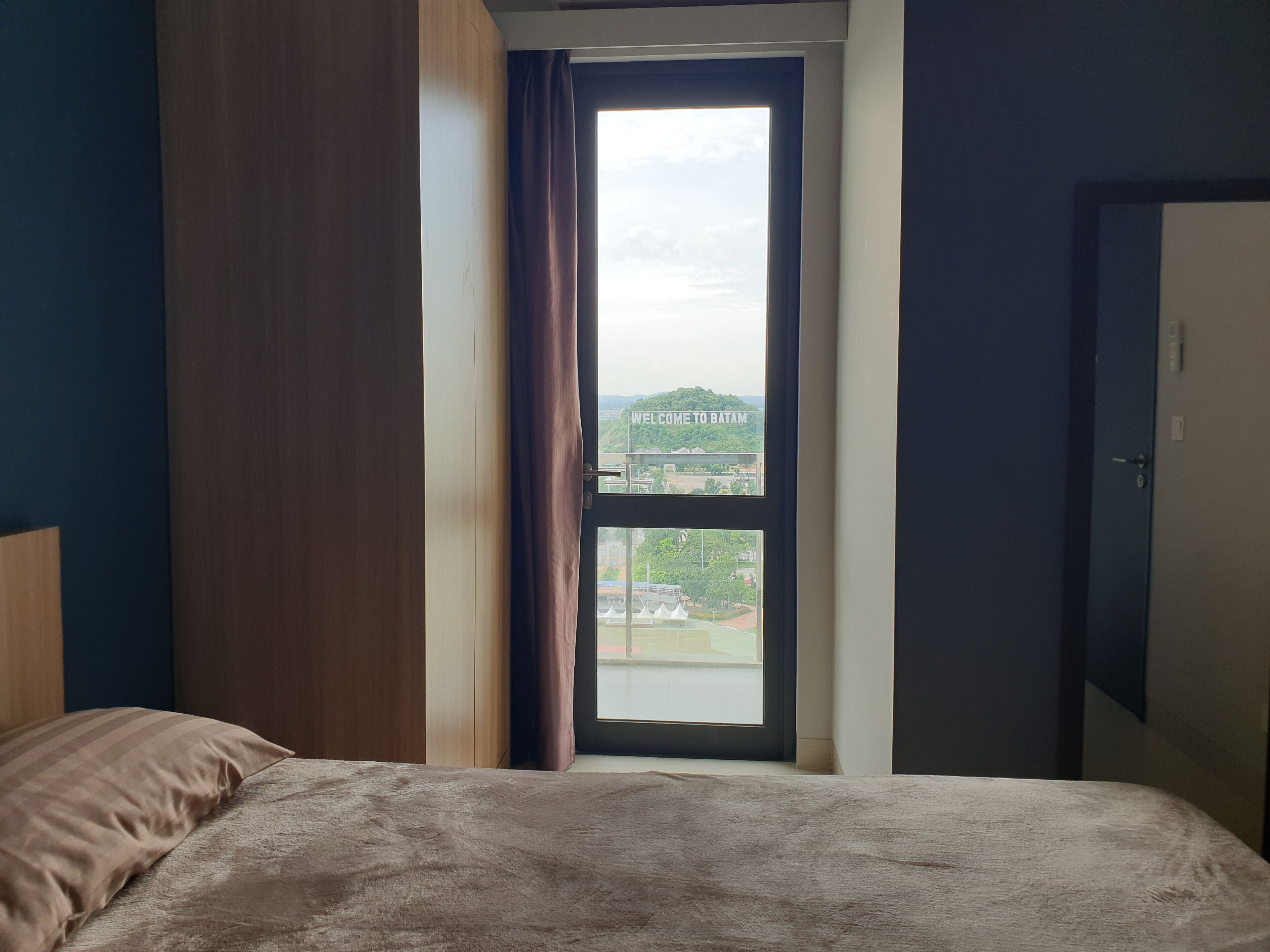 A bedroom with a bed, a window with a view of a cityscape, and a door.
