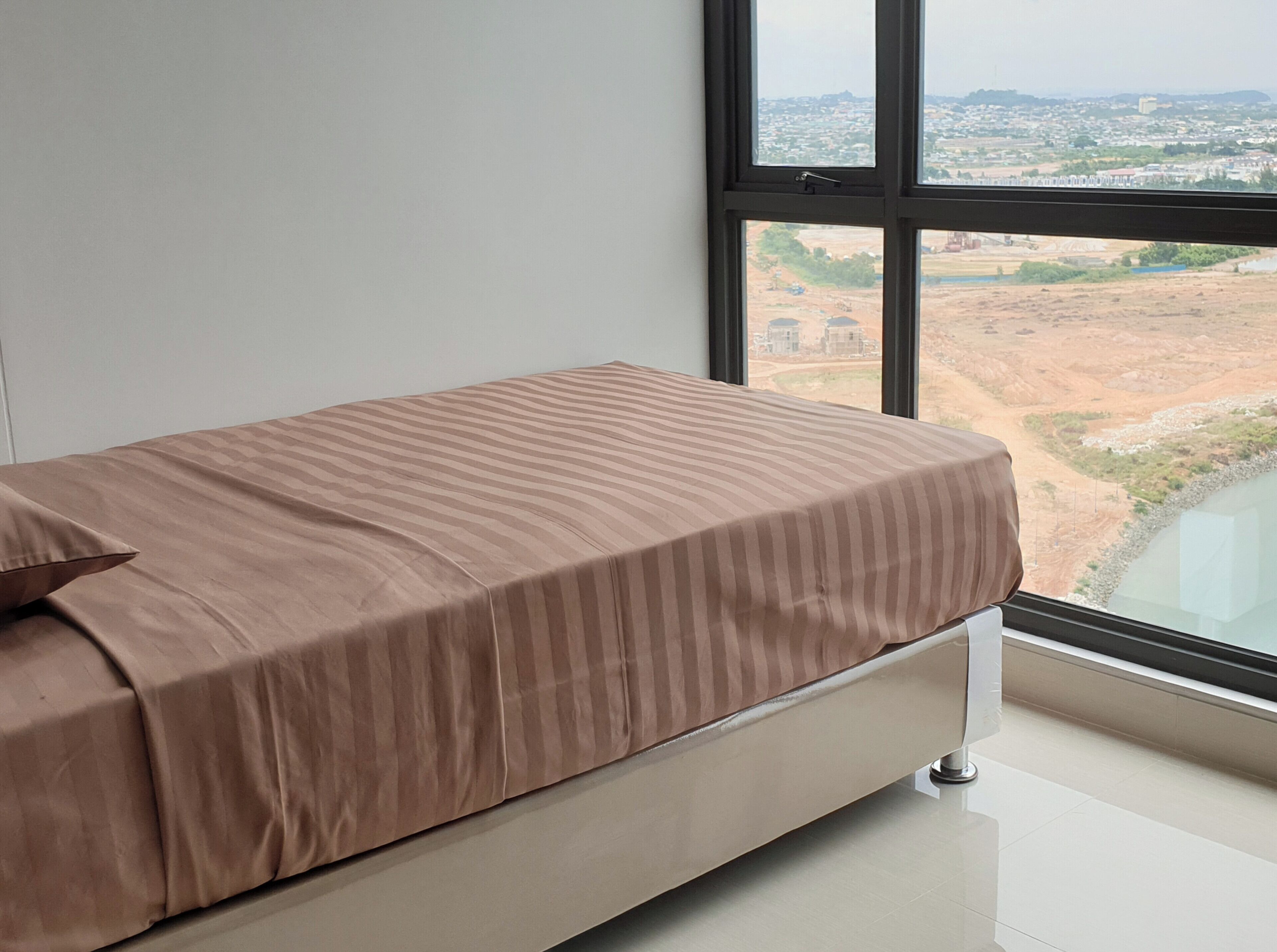 Una cama individual con colcha a rayas en una habitación con un ventanal grande que da a un paisaje.