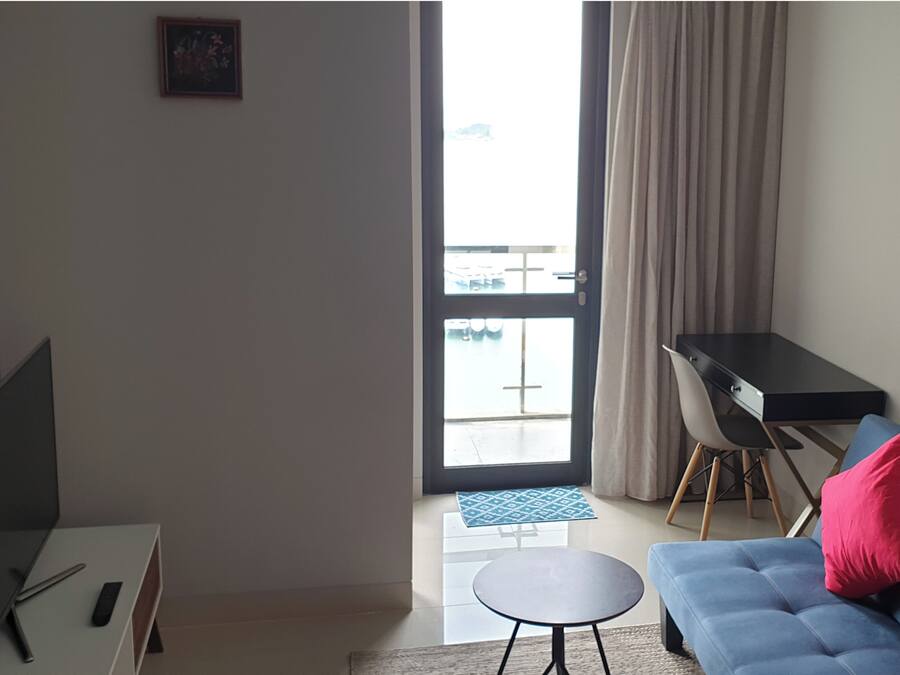 Een moderne woonkamer met een bank, een klein rond tafeltje, een bureau en uitzicht op een balkon met een hekwerk.
