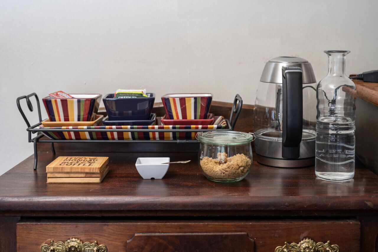 A wooden table with a coffee maker, a glass jar, and colorful striped cups.