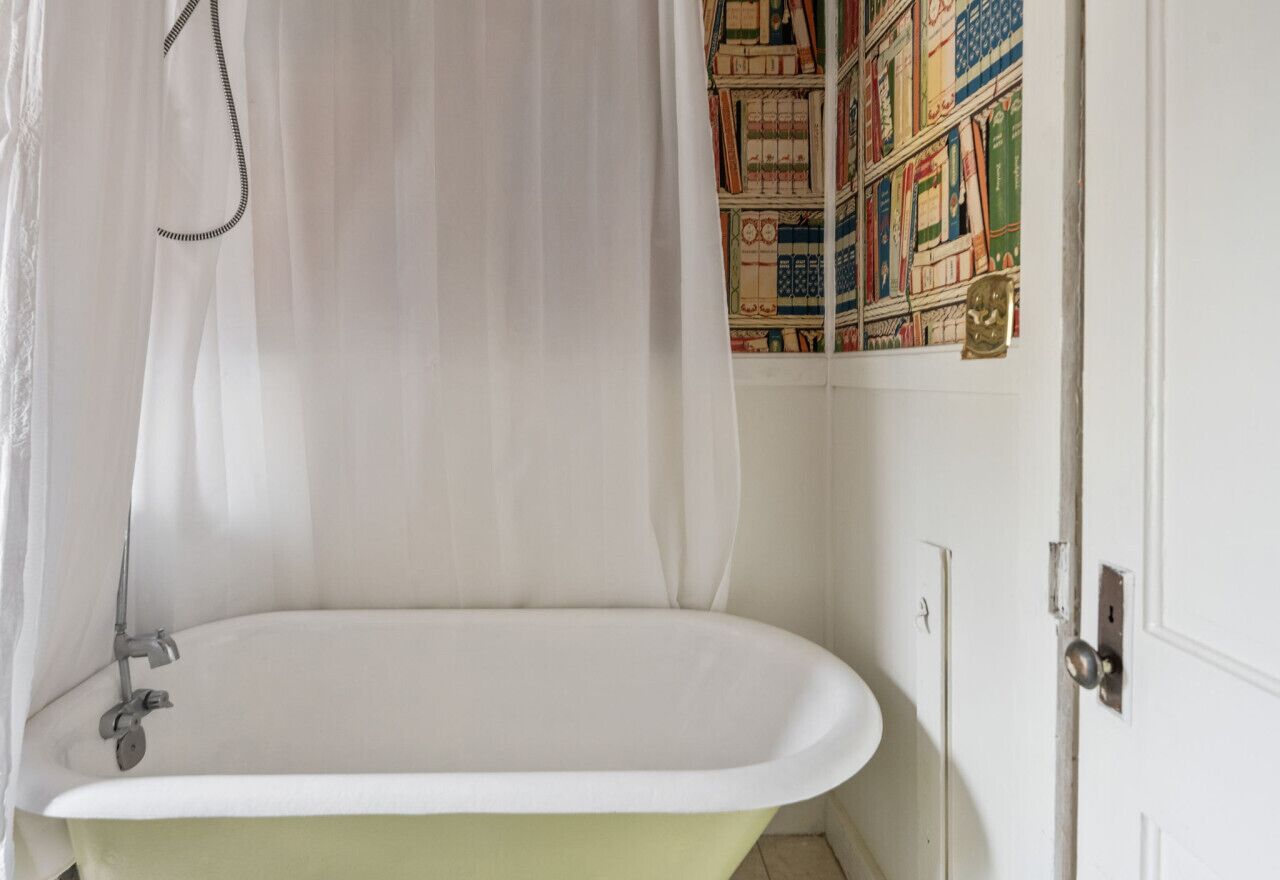 Ein Badezimmer mit einer freistehenden Badewanne, einer Duschvorhang und einem an der Wand befestigten Bücherregal.