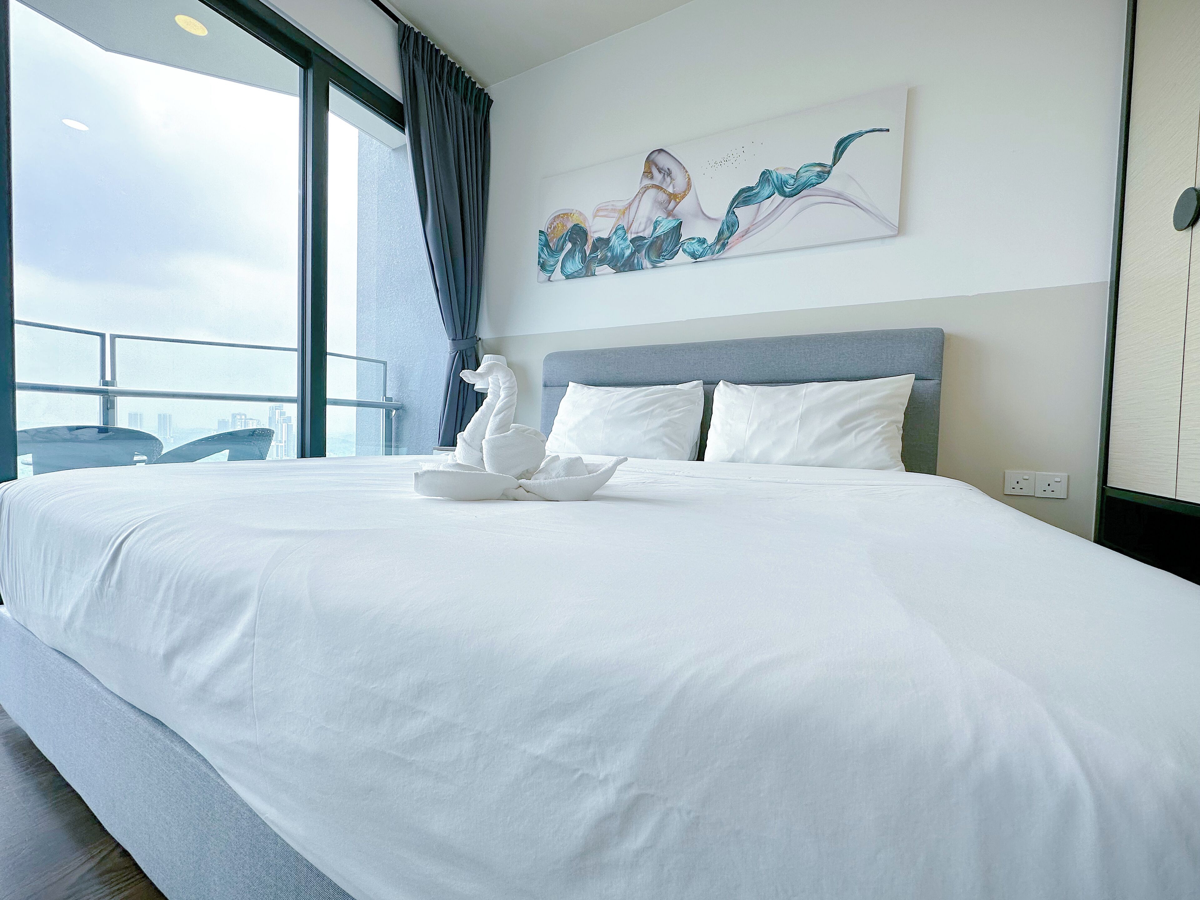 Ein Hotelzimmer mit einem großen Bett, einem Gemälde an der Wand und Blick auf die Stadt durch das Fenster.