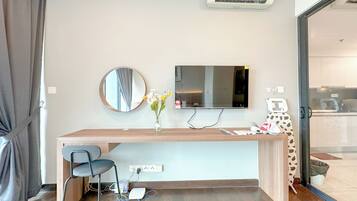 A modern hotel room with a wooden desk, a chair, a flat-screen TV, a mirror, and a vase with flowers.