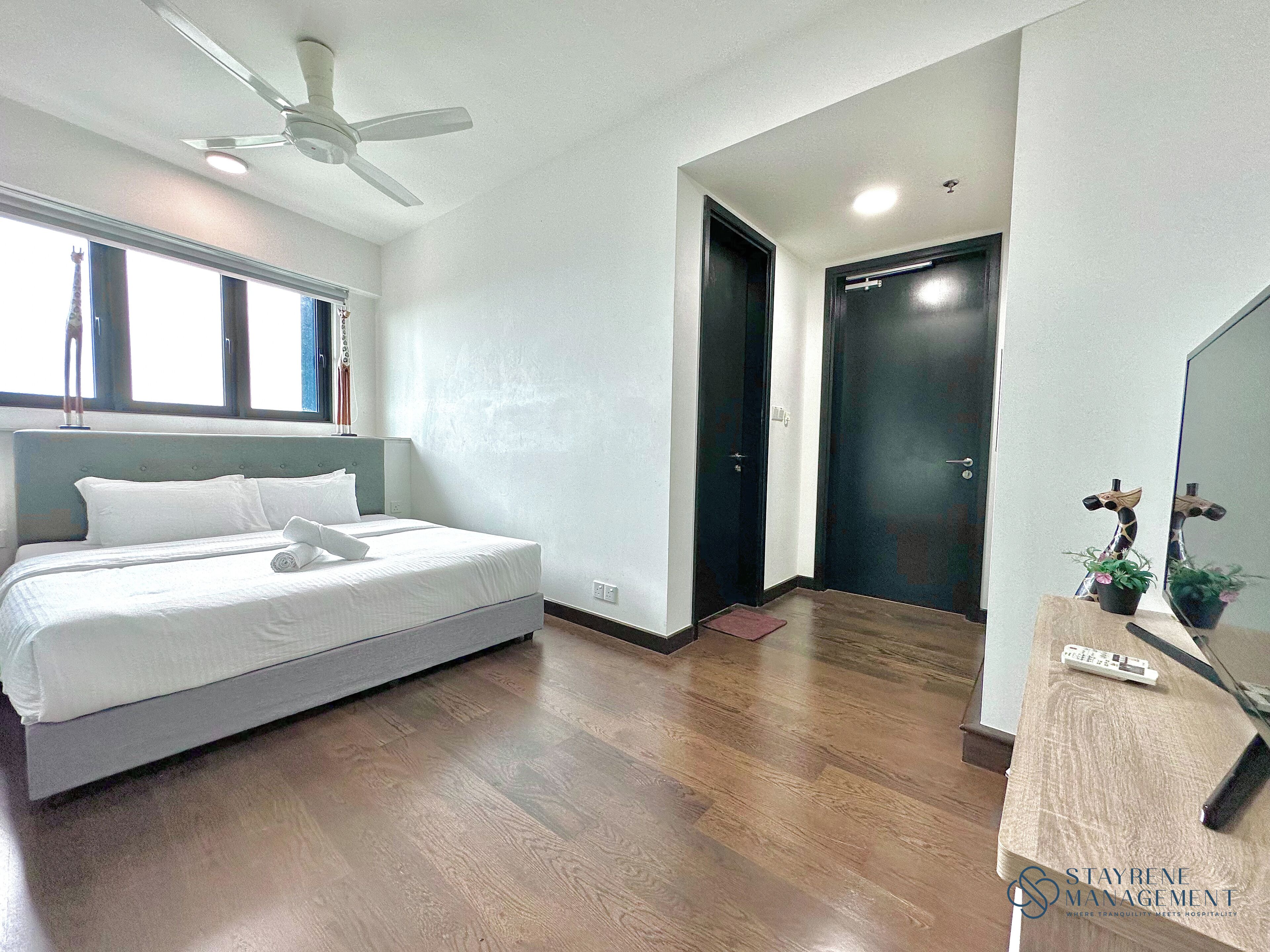 A hotel room with a bed, a ceiling fan, a door, and a small plant on the nightstand.