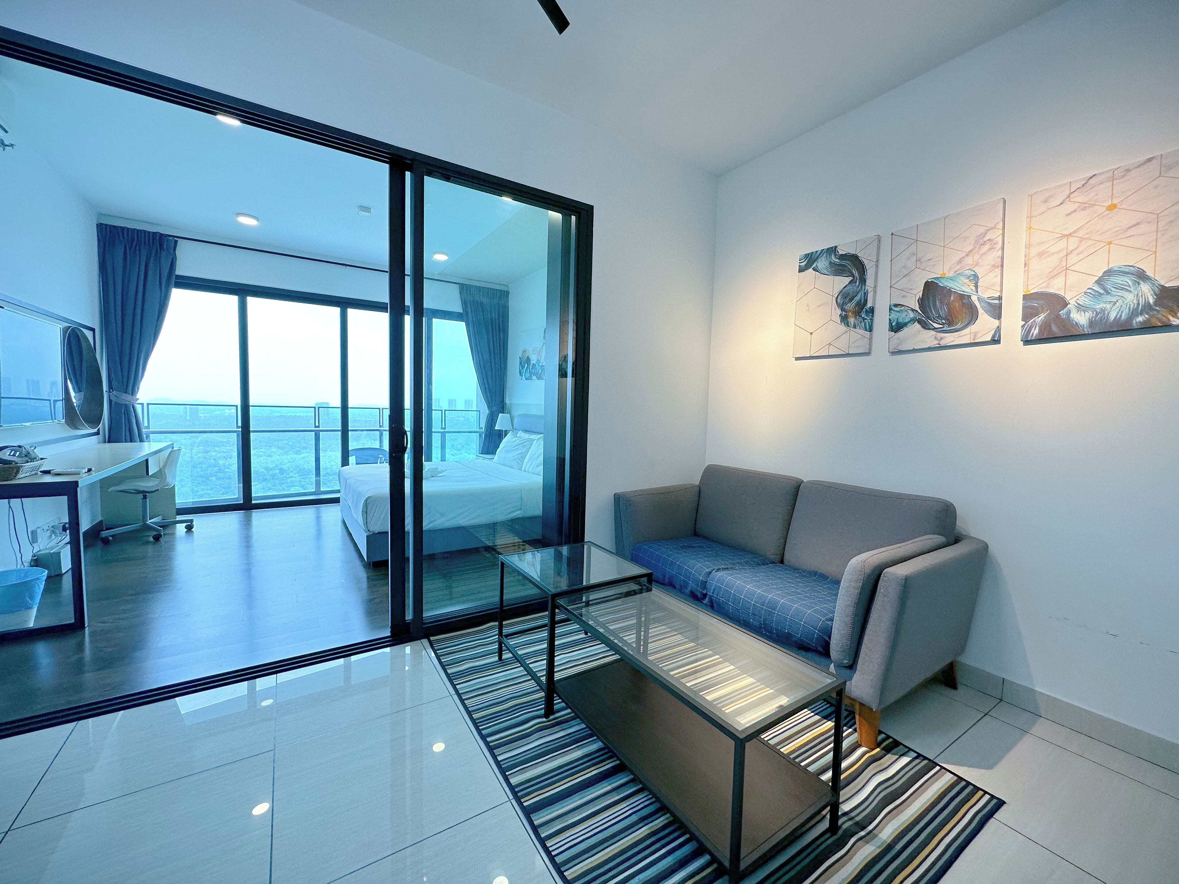 A modern hotel room with a glass partition, a sofa, a glass coffee table, and artwork on the wall.