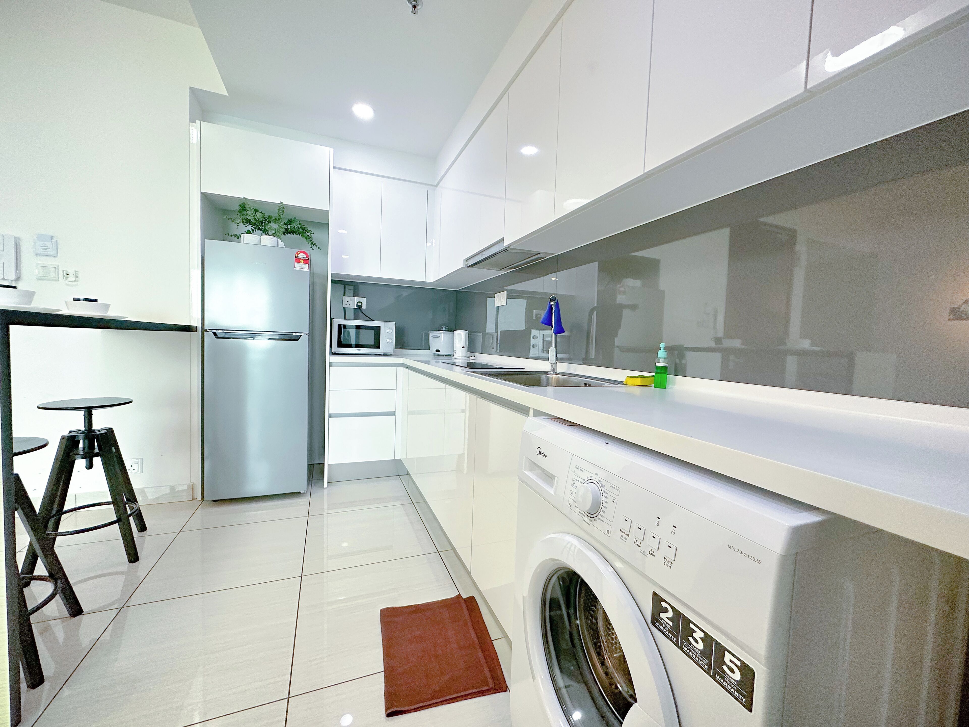 Une cuisine moderne avec des meubles blancs, un réfrigérateur en acier inoxydable, un four à micro-ondes, un évier et un lave-linge.
