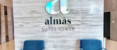 Un vestíbulo de hotel con un gran letrero que dice "almás SUITES TOWER" y dos sillas azules con una pequeña mesa frente a ellas.